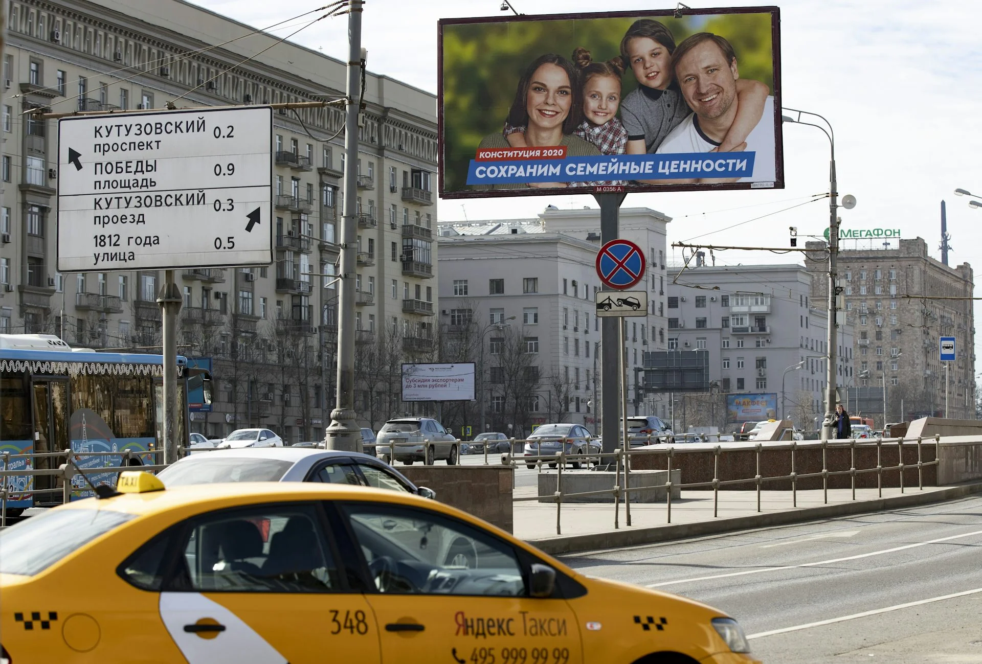A yellow taxi drives past a billboard with a photo of a smiling woman, man and two children.