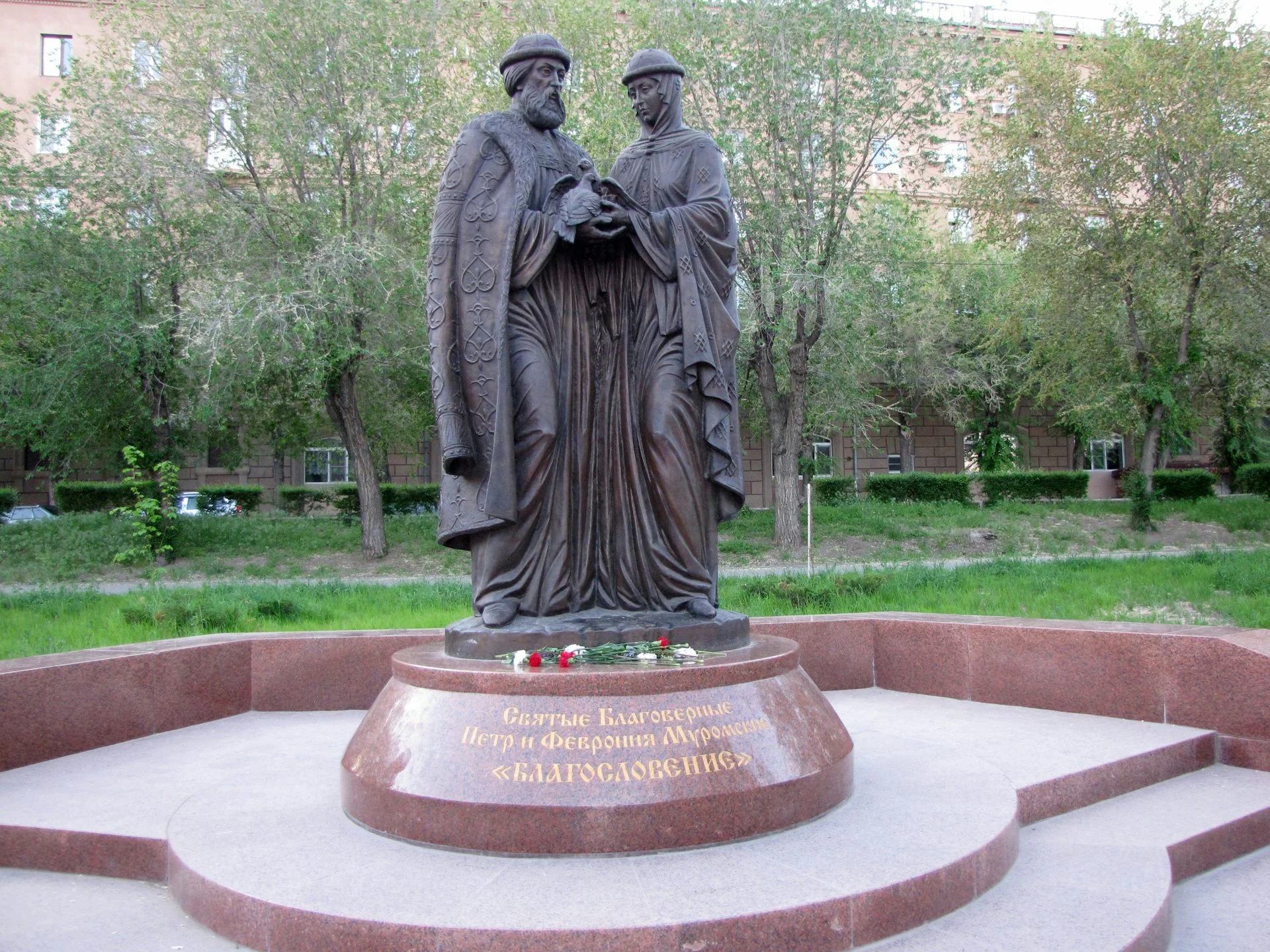 A statute of a man and woman in long robes facing each other and holding a pair of birds.