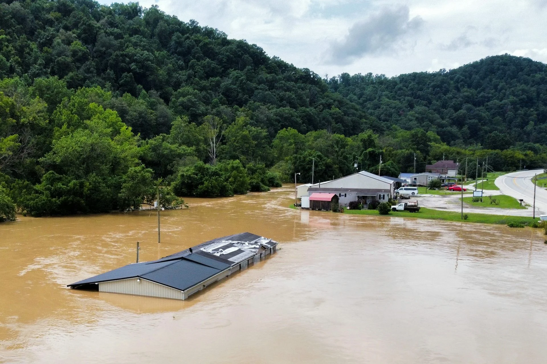 Muddy water up to the roofline of one house and at the edges of others along a river.