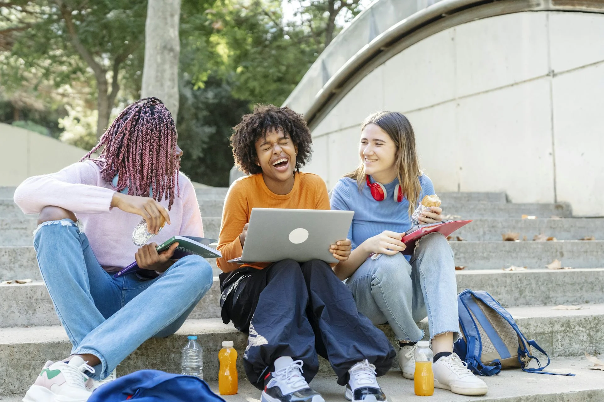 Three young people sit on steps together and smile.