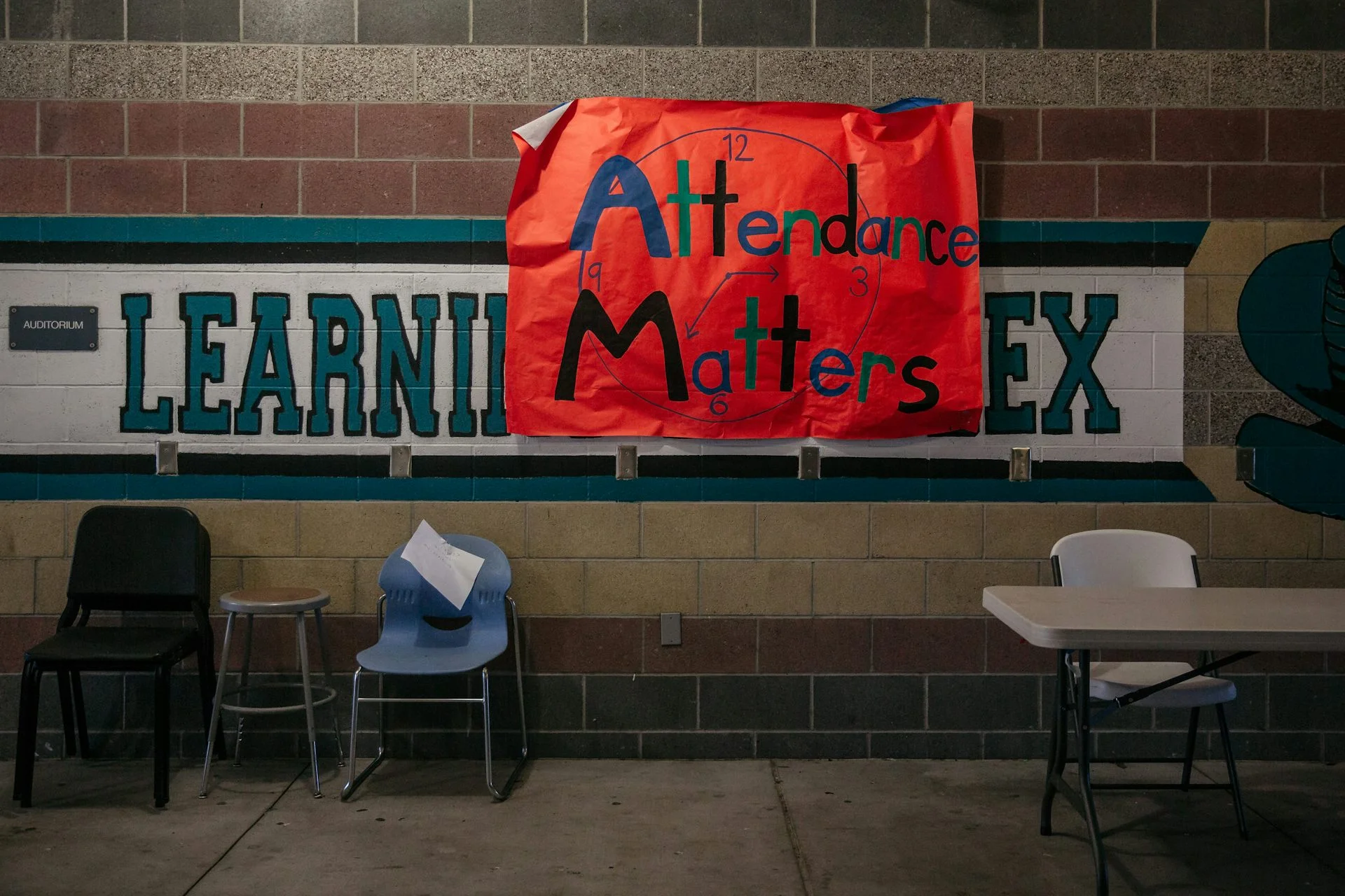 A hand-drawn red sign that says 'Attendance matters' is hung on a tile wall with chairs nearby.