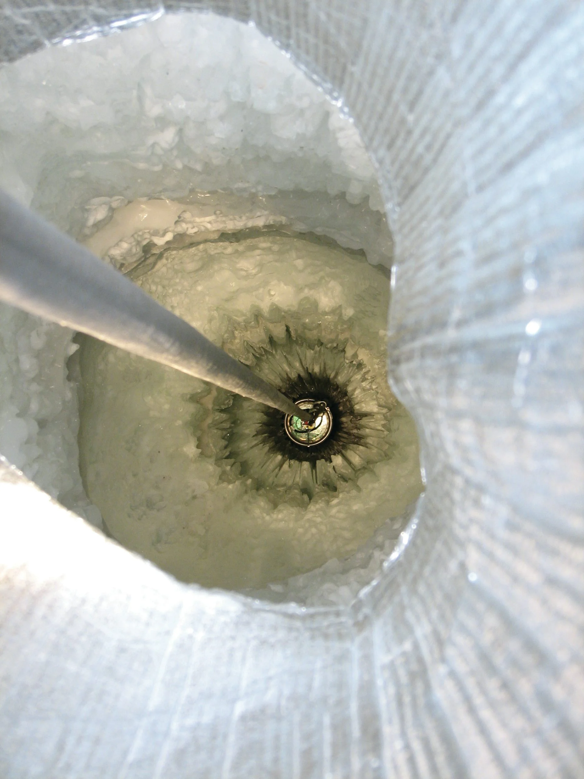 A tether descends into a vertical tunnel through snowy ice.