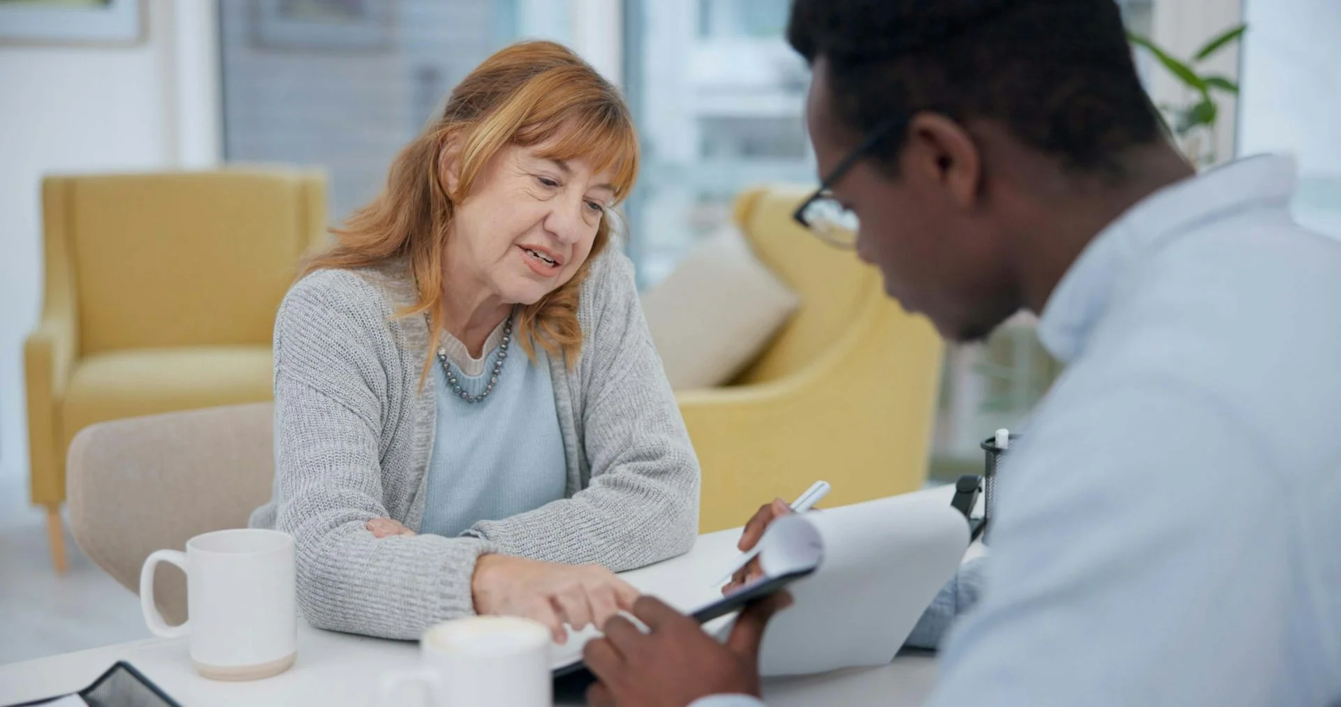 A woman sits across the table from a man who is showing her something on a clipboard.