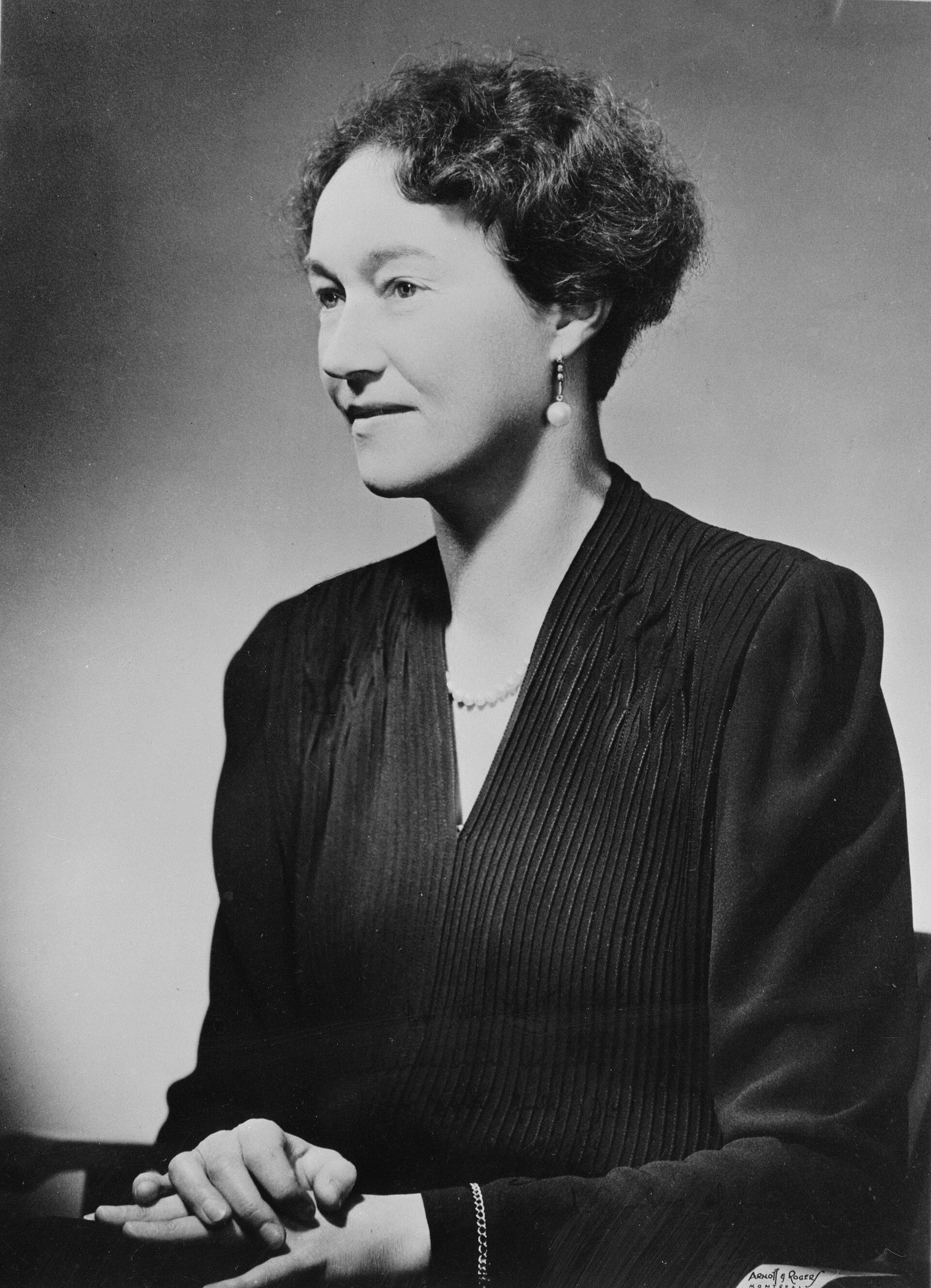 A black and white portrait of a woman in a black dress and pearls.