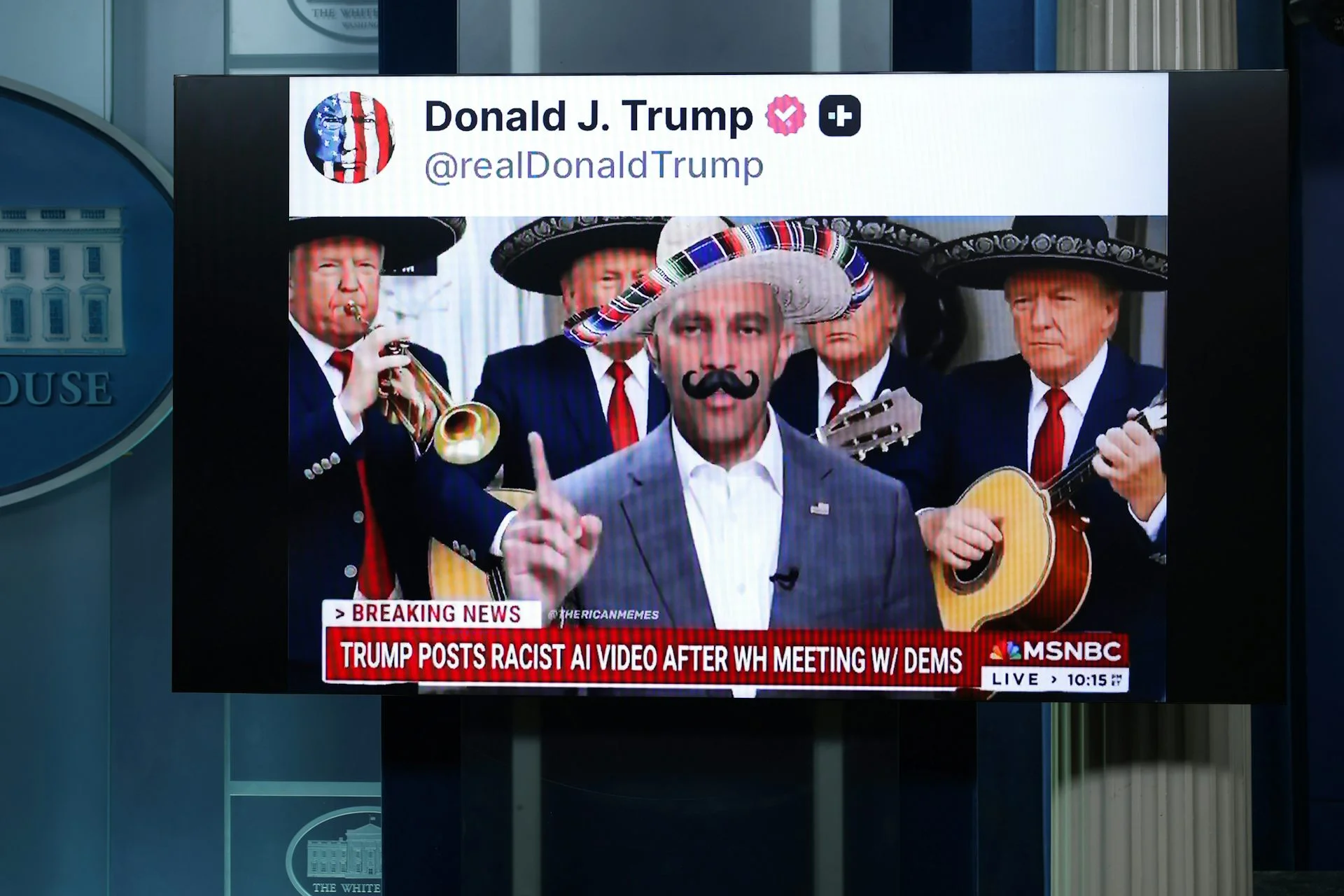 A screen in a press briefing room shows a social media video of a man in a sombrero and fake mustache, flanked by mariachi musicians, above a cable news banner.